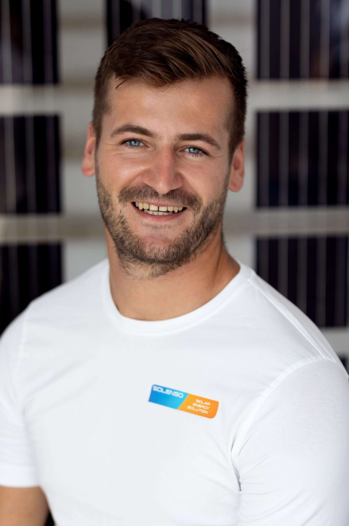 Lächelnder Mitarbeiter von Solenso Solar vor Photovoltaik-Modulen.